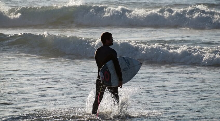 Homem Na Camisa Preta Segurando A Prancha De Surf Branca Nas Ondas Do Mar Durante O Dia CmyowX SAD8