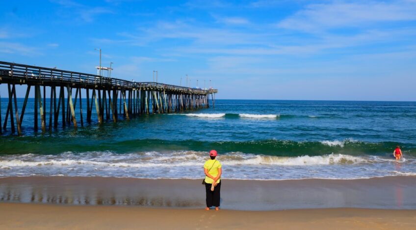 Um Homem Em Cima De Uma Praia De Areia Ao Lado Do Oceano DDFSaq7TUxc
