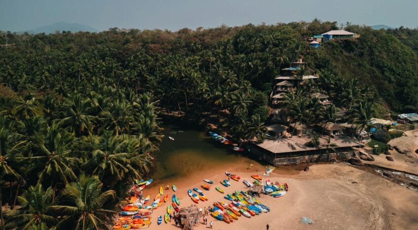 Explore the vibrant kayaks and serene beach backdrop at Sacral Beach, Goa, from a captivating aerial perspective.