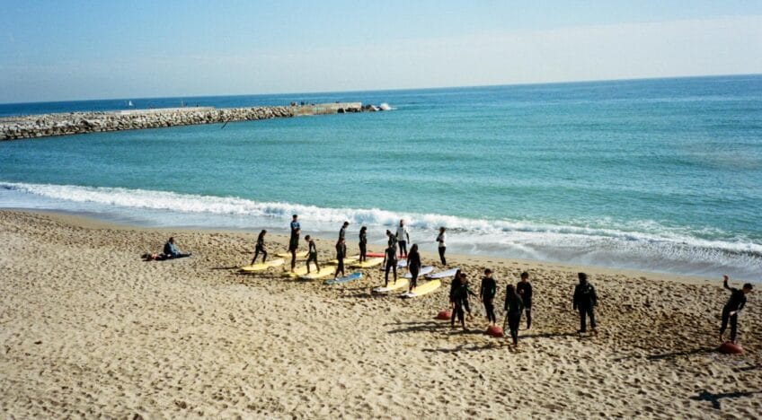 A group of surfers in wetsuits practicing on surfboards at a sunny beach.